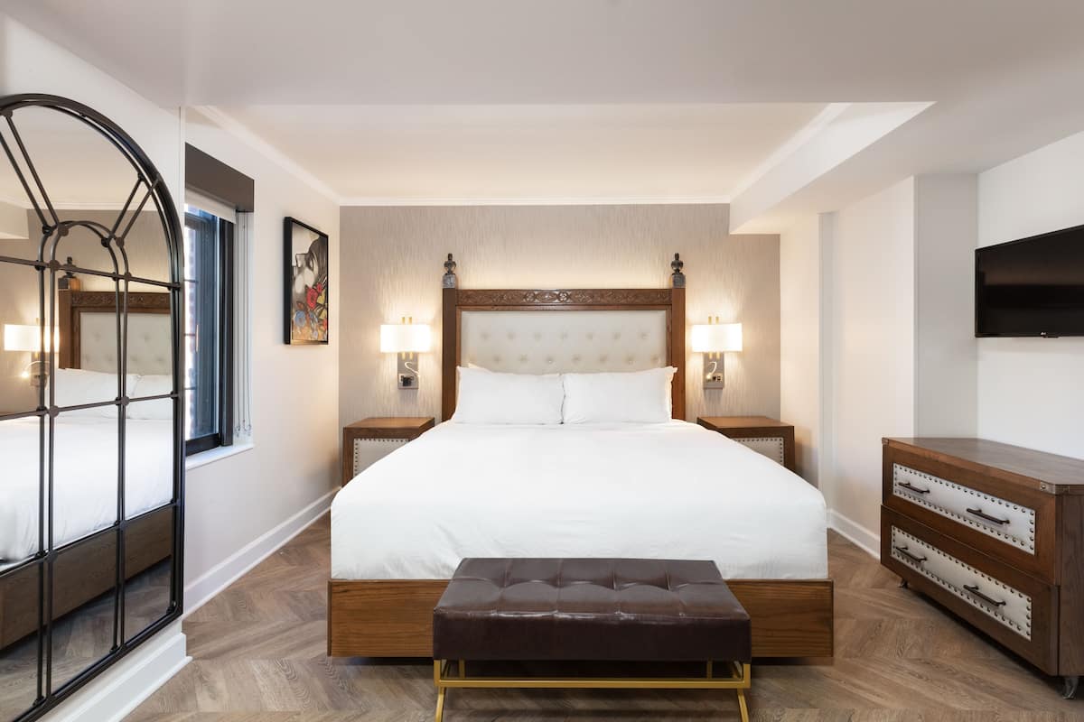 A hotel room with a large bed, bedside lamps, a TV, and a wooden dresser.