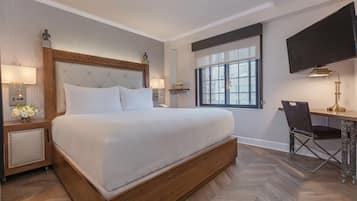 A hotel room with a large bed, a desk with a chair, a television, and a window with a view.