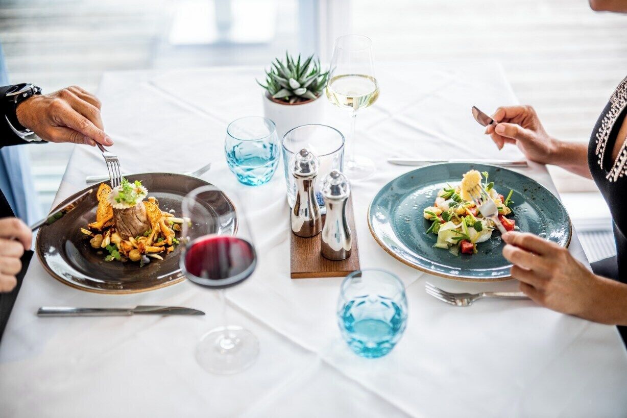A dining table with two plates of food, glasses of wine, and a small plant.