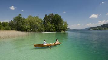 A clear lake with a boat carrying two people, surrounded by trees and distant hills.