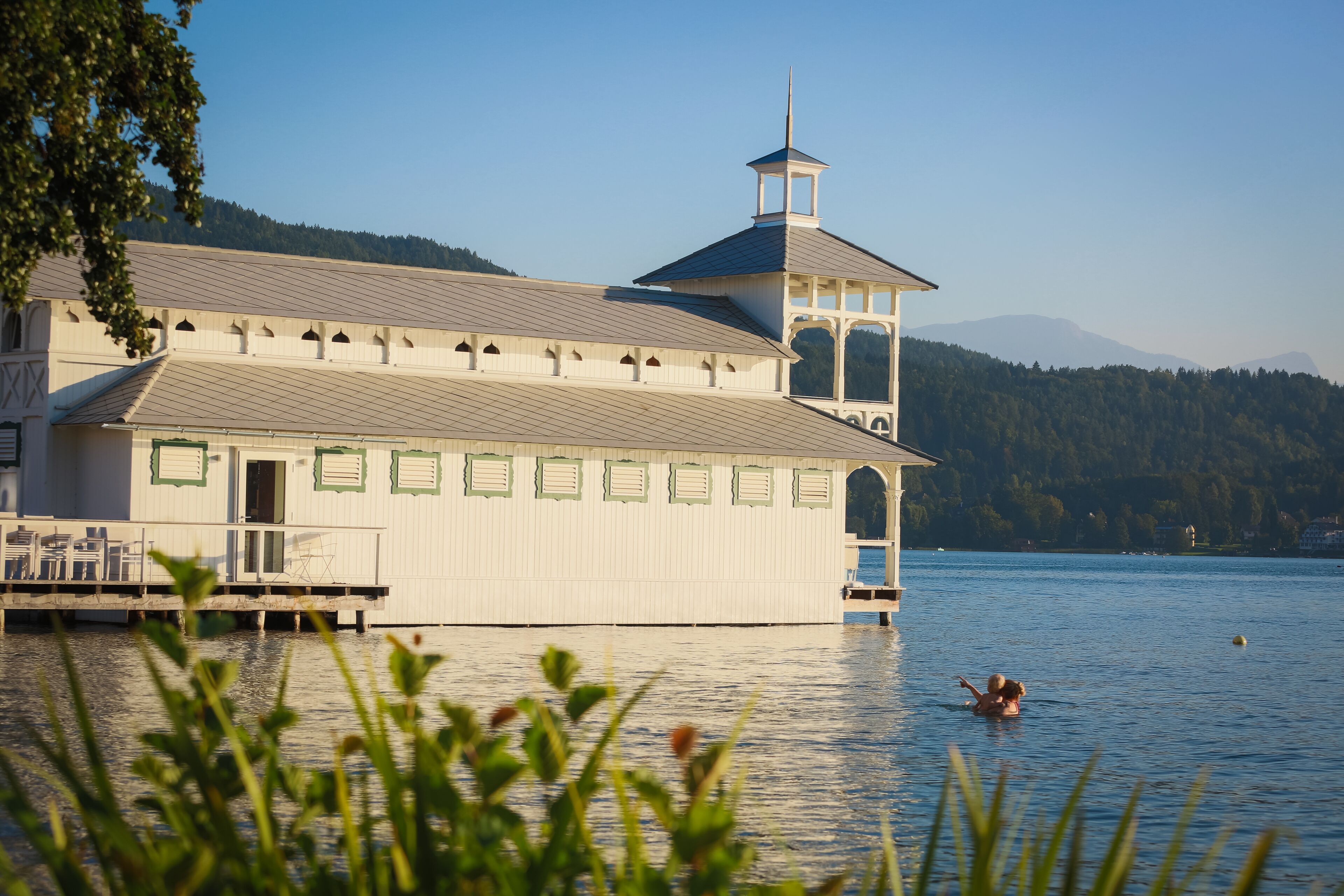 A large building with a tower, a dock, and a person swimming in the water.