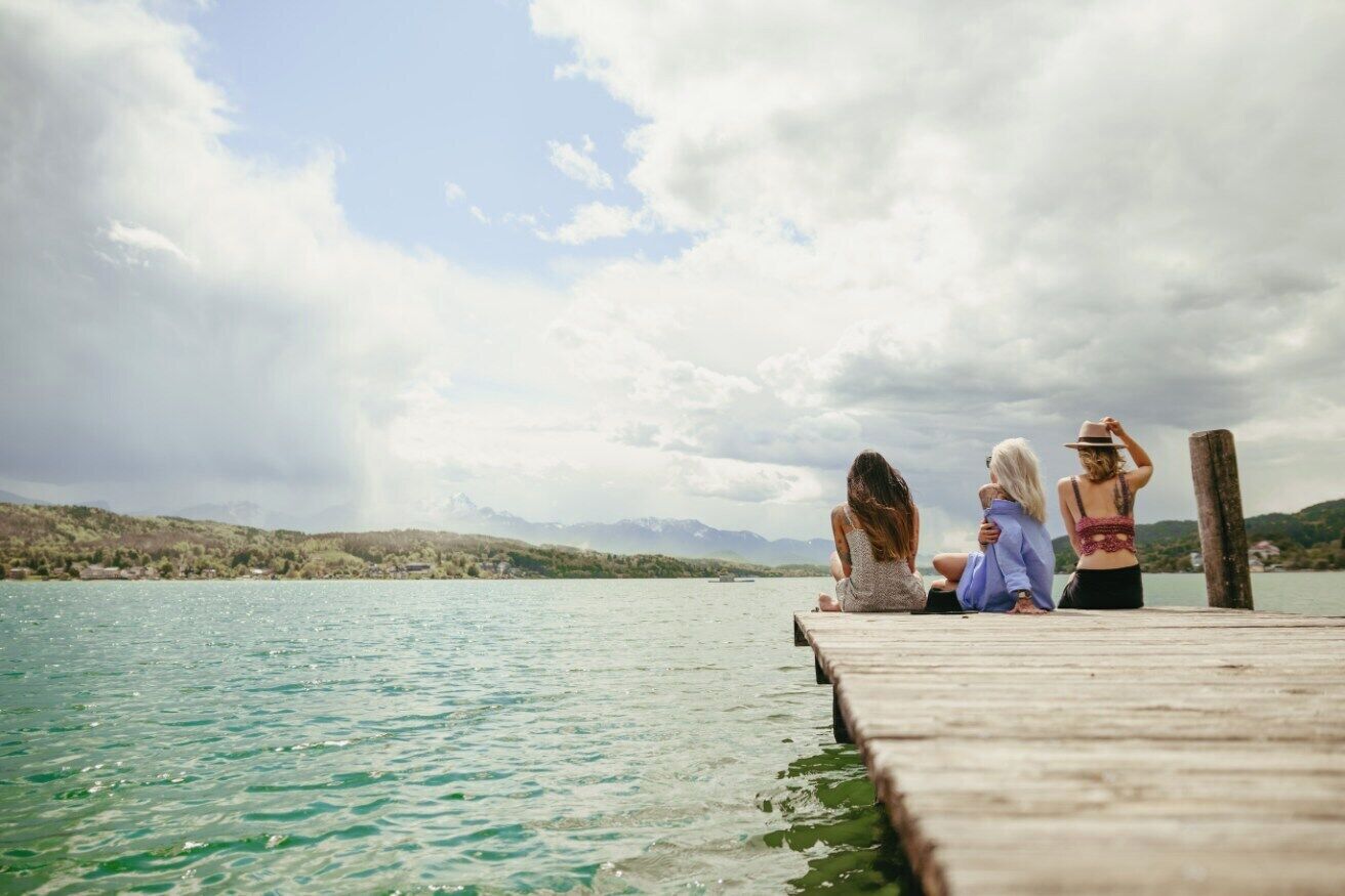 Un muelle de madera se adentra en un lago tranquilo con montañas al fondo.