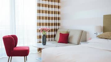 A hotel room with a large bed, a red armchair, a small round table, and a vase of flowers.