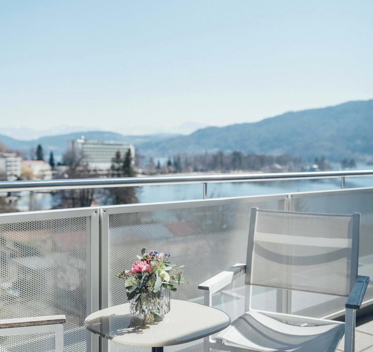 A balcony with a table and chairs, overlooking a body of water and mountains.