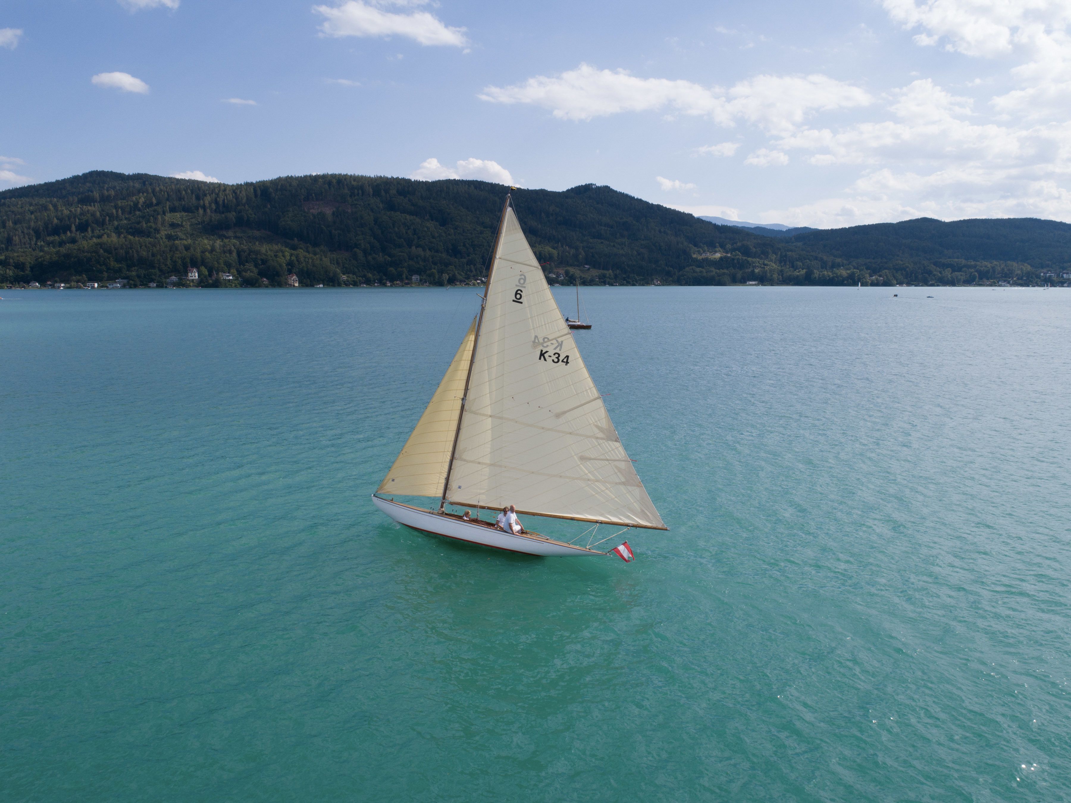 A sailboat on a calm lake with a forested mountain in the background.