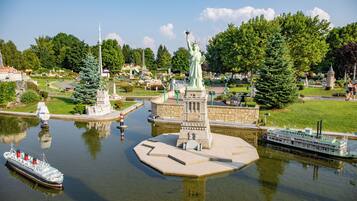 A model of the Statue of Liberty on a small island, surrounded by water, with a replica of a steamboat and a tower in the background.