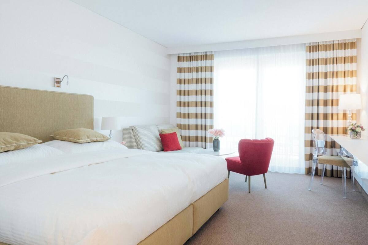 A hotel room with a large bed, a desk with a chair, and a window with striped curtains.