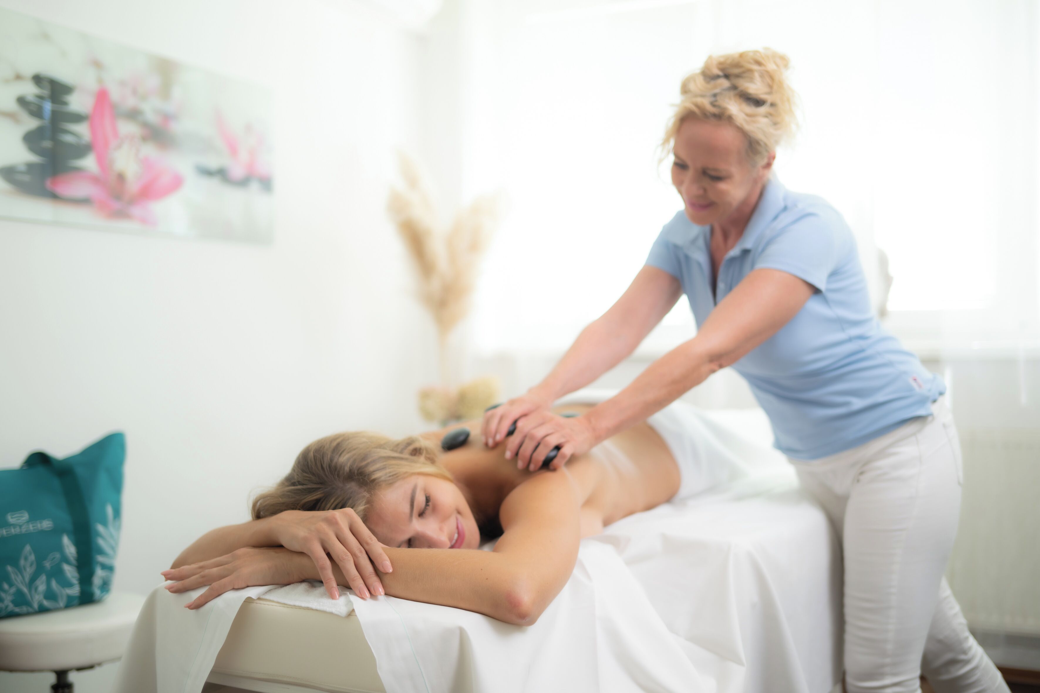 A massage therapy session in a room with a bed, a massage table, and a wall with a painting.