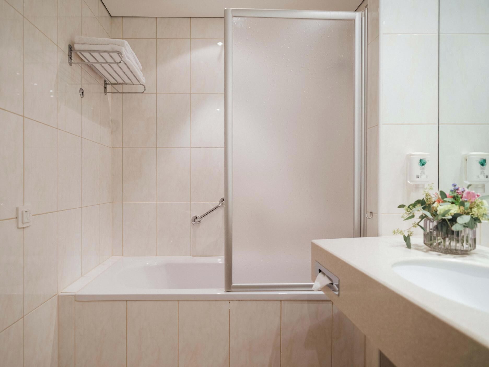 Ein modernes Badezimmer mit einer Badewanne, einer Dusche mit Glastür, einem Handtuchhalter und einem Waschbecken mit Blumen.'