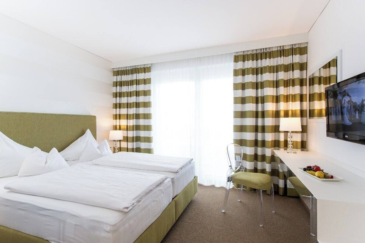 A hotel room with a bed, a desk with a chair, a television, and curtains.