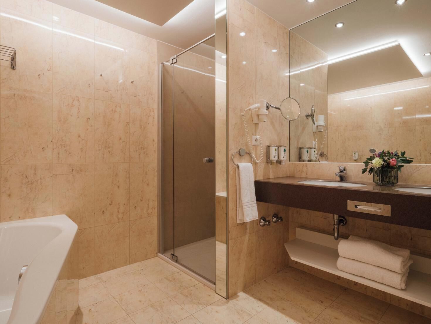 A modern bathroom with a glass-enclosed shower, a large mirror, and a dark countertop with a sink and towel rack.