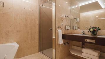A modern bathroom with a glass-enclosed shower, a large mirror, and a dark countertop with a sink and towel rack.