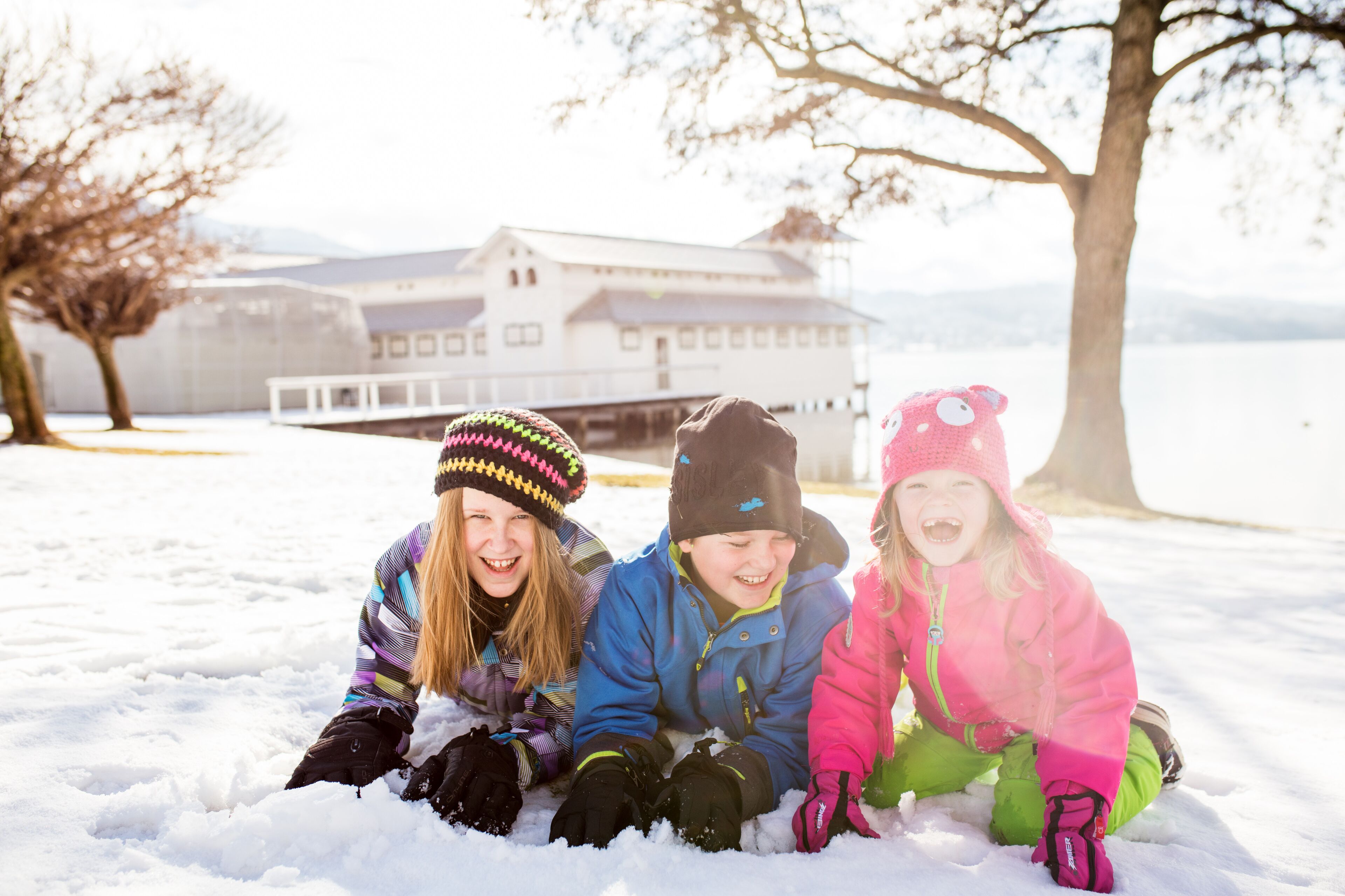 Trois enfants jouent dans la neige, avec un grand bâtiment en arrière-plan.