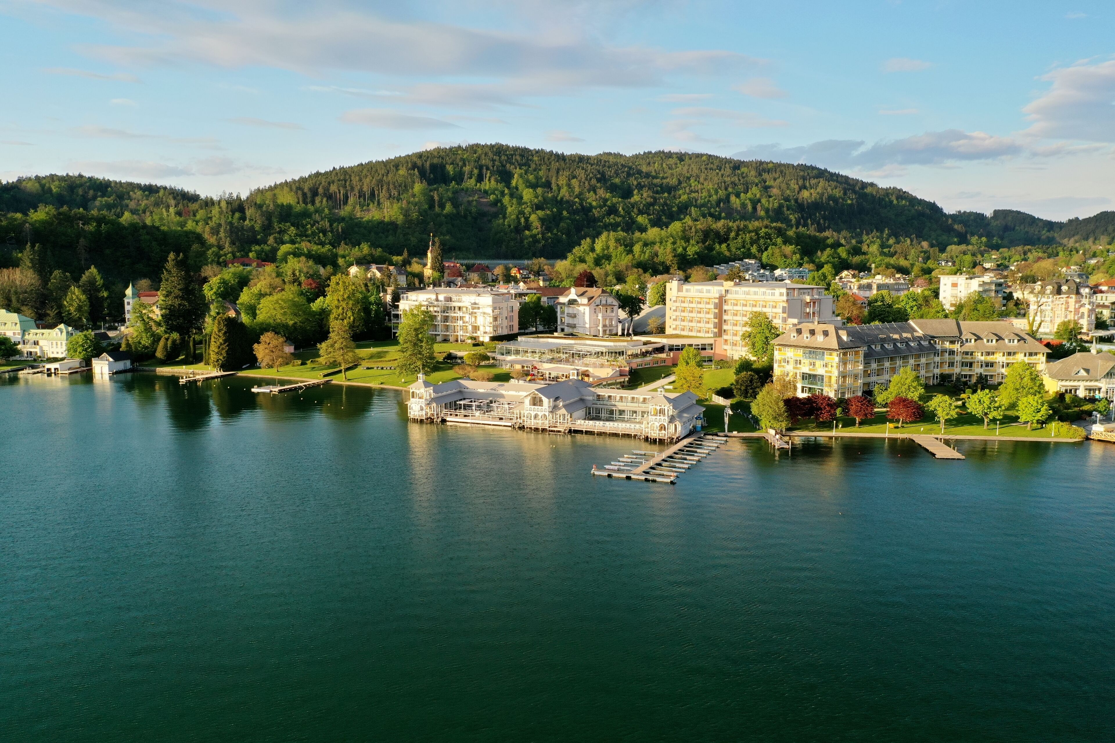 Un hôtel situé au bord d’un lac, composé de plusieurs bâtiments, doté d’un quai et surplombant une colline boisée.