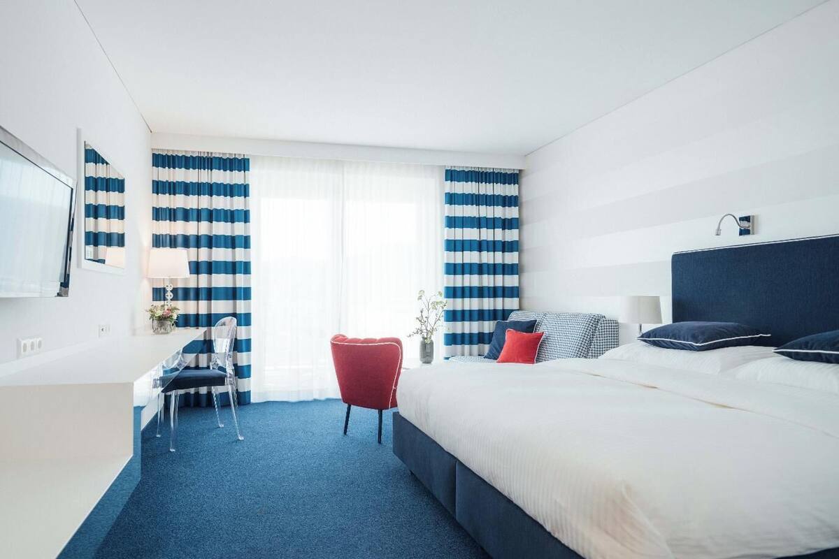 A modern hotel room with a large bed, a desk, and a red chair.