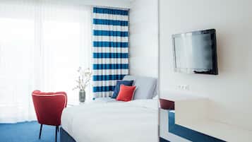 A hotel room with a bed, a TV, a red chair, and a striped curtain.