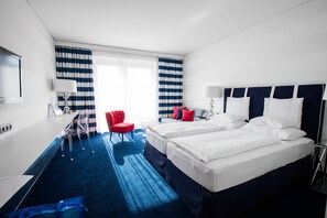 A hotel room with two beds, a desk, a chair, and a large window with curtains.
