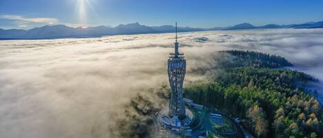 A tower surrounded by a forest and clouds, with a clear sky and mountains in the background.