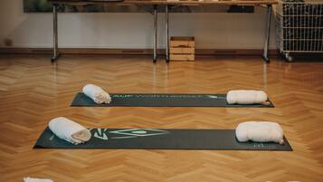 A room with wooden flooring, yoga mats, towels, a table with a Buddha statue, and a painting of a Buddha.