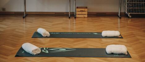 Una habitación con suelo de madera, tapetes de yoga, toallas, una mesa con una estatua de Buda y un cuadro de Buda.