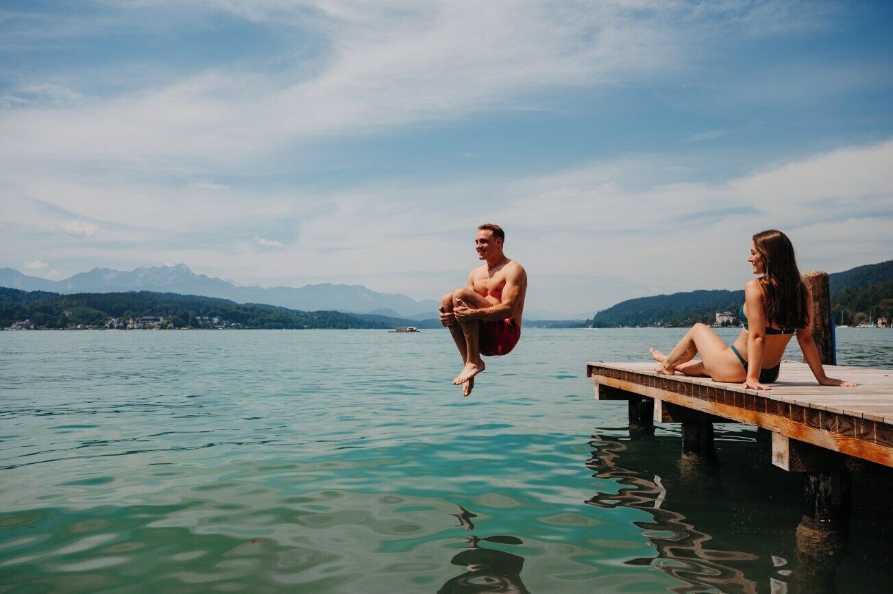 A wooden dock extending into a calm lake with mountains in the background.