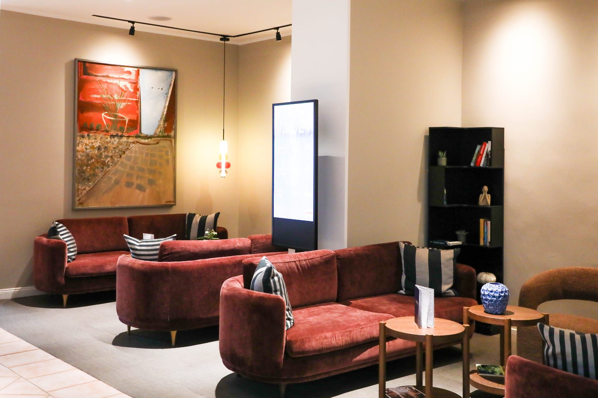 Een moderne woonkamer met een rode zithoek, een zwarte boekenkast en een groot abstract schilderij aan de muur.