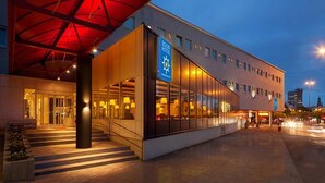 Un hôtel moderne doté d’une façade en verre, d’un auvent rouge bien visible et d’une enseigne indiquant qu’il s’agit d’un hôtel.