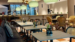 Un intérieur de restaurant moderne avec de hautes tables, des chaises en osier et des lampes suspendues.