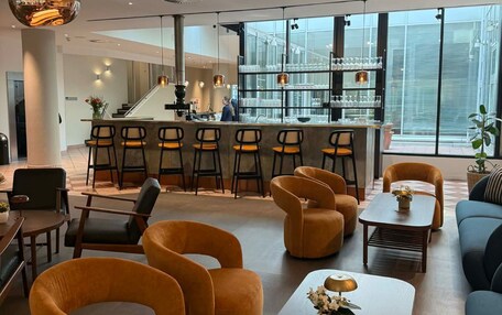 A modern hotel lobby with a bar area, seating, and large windows.