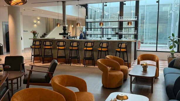 Un hall d’hôtel moderne doté d’un bar, de coins salon et de grandes fenêtres.