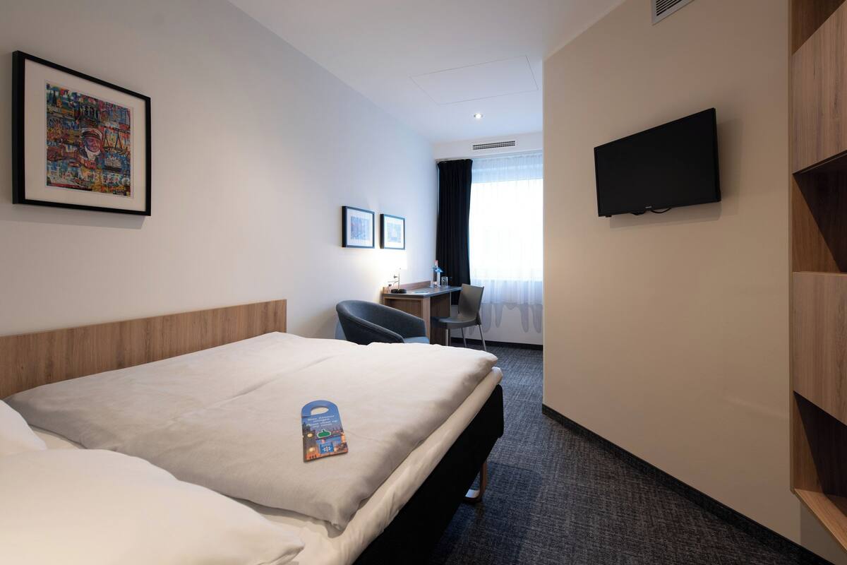 Une chambre d’hôtel avec un lit, un bureau, une chaise, une télévision et un tableau encadré au mur.