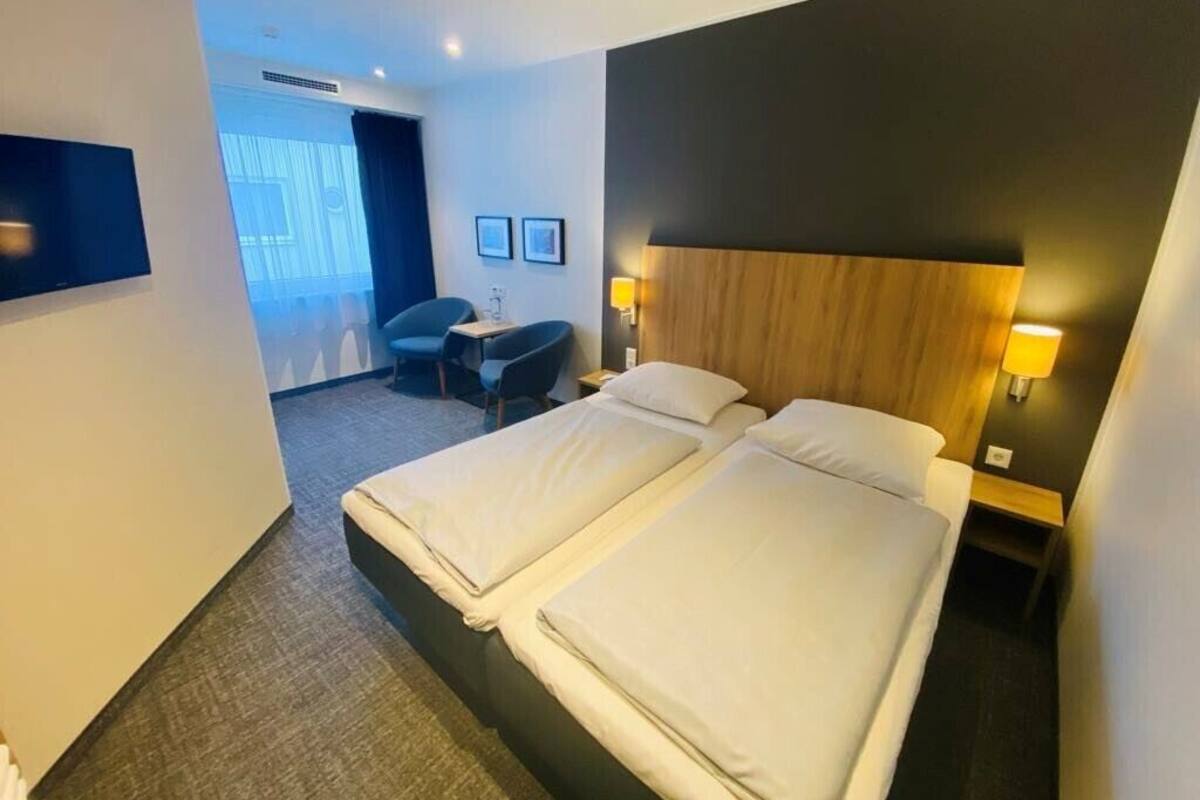 Une chambre d’hôtel avec deux lits, un bureau, une chaise et un téléviseur.