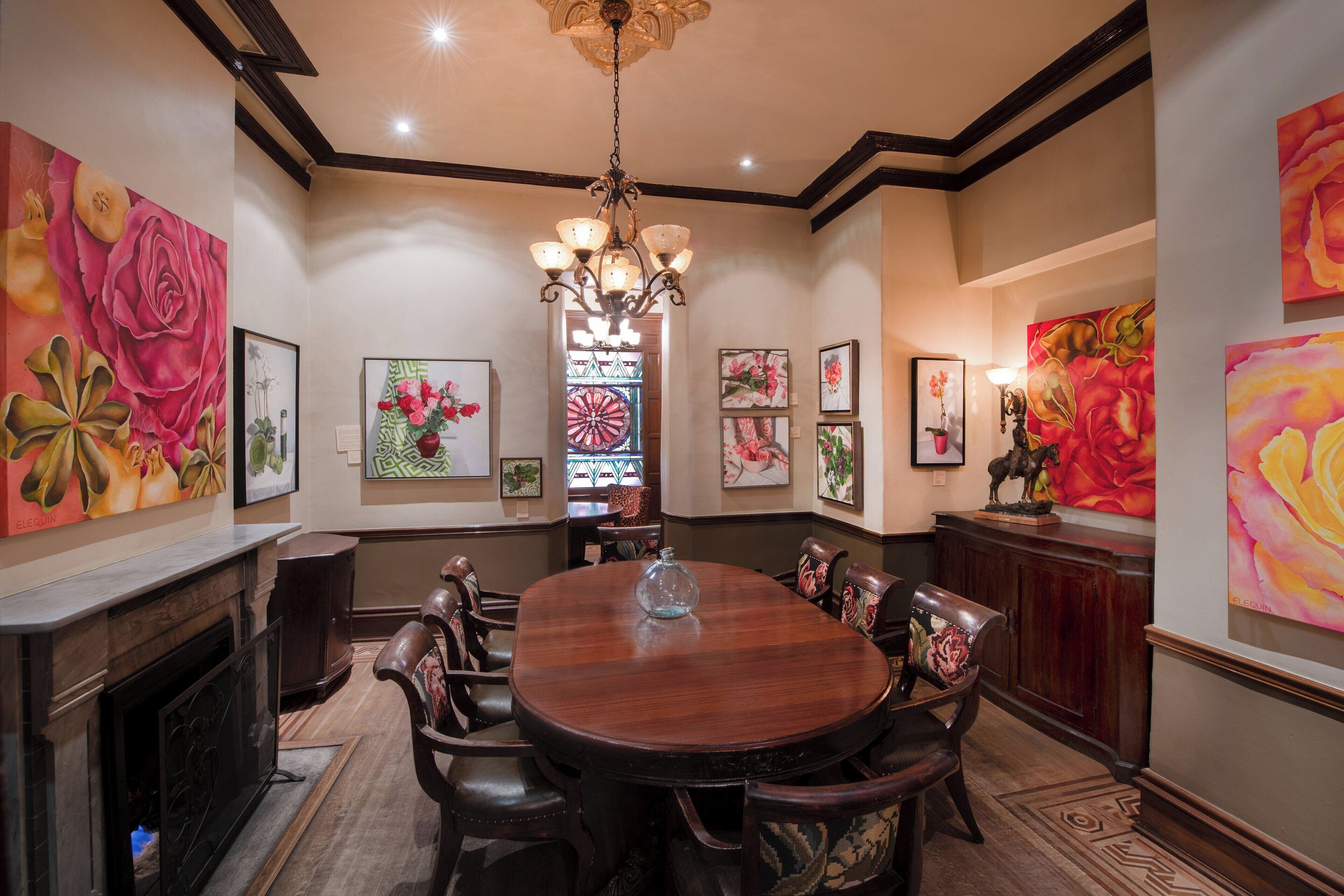 A dining room with a round table, chairs, a chandelier, and floral artwork on the walls.