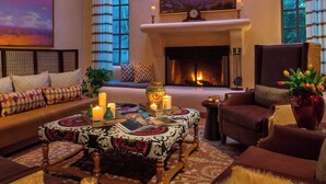 A cozy living room with a fireplace, comfortable seating, a chandelier, and a large painting of a sunset. - La Posada de Santa Fe, A Tribute Portfolio Resort & Spa by Marriott (Santa Fe)
