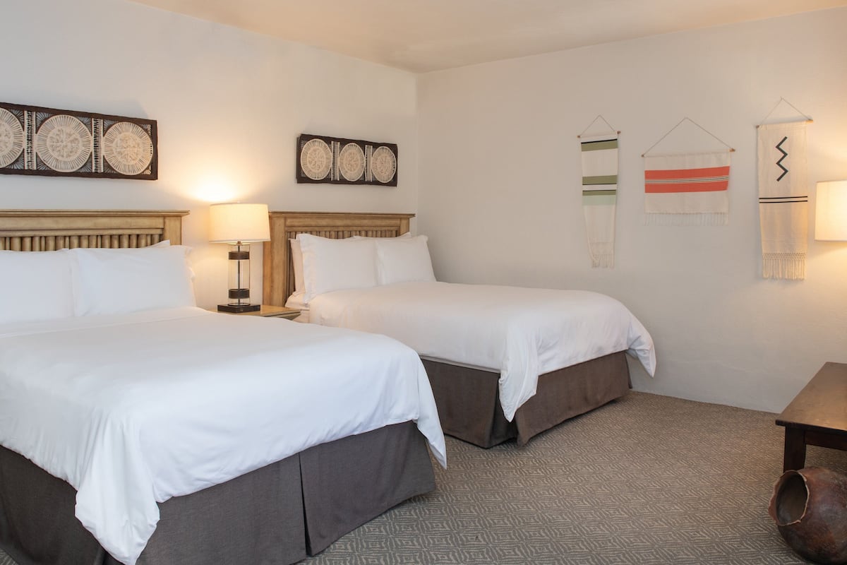 A hotel room with two beds, a nightstand, a lamp, and decorative wall hangings.