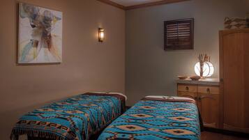 A room with two beds, a wall-mounted light, a window with blinds, and a wooden cabinet.