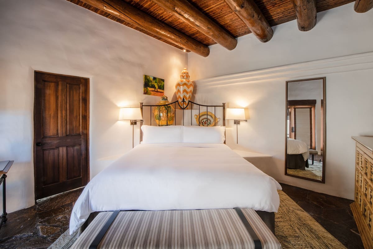 A bedroom with a large bed, wooden door, and a mirror on the wall.