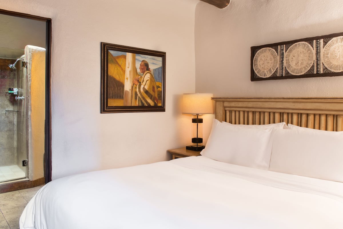 A hotel room with a bed, a painting, a lamp, and a shower.