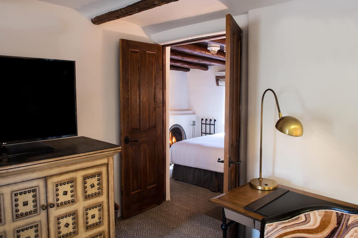 A hotel room with a wooden cabinet, a flat-screen TV, a bed with a white comforter, a bedside lamp, and a patterned rug.