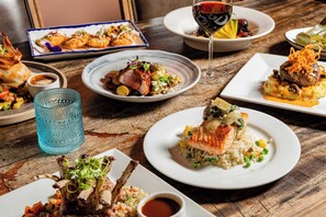 A variety of dishes on a wooden table, including a plate with salmon and rice, another with a steak and vegetables, and a glass of red wine. - La Posada de Santa Fe, A Tribute Portfolio Resort & Spa by Marriott (Santa Fe)