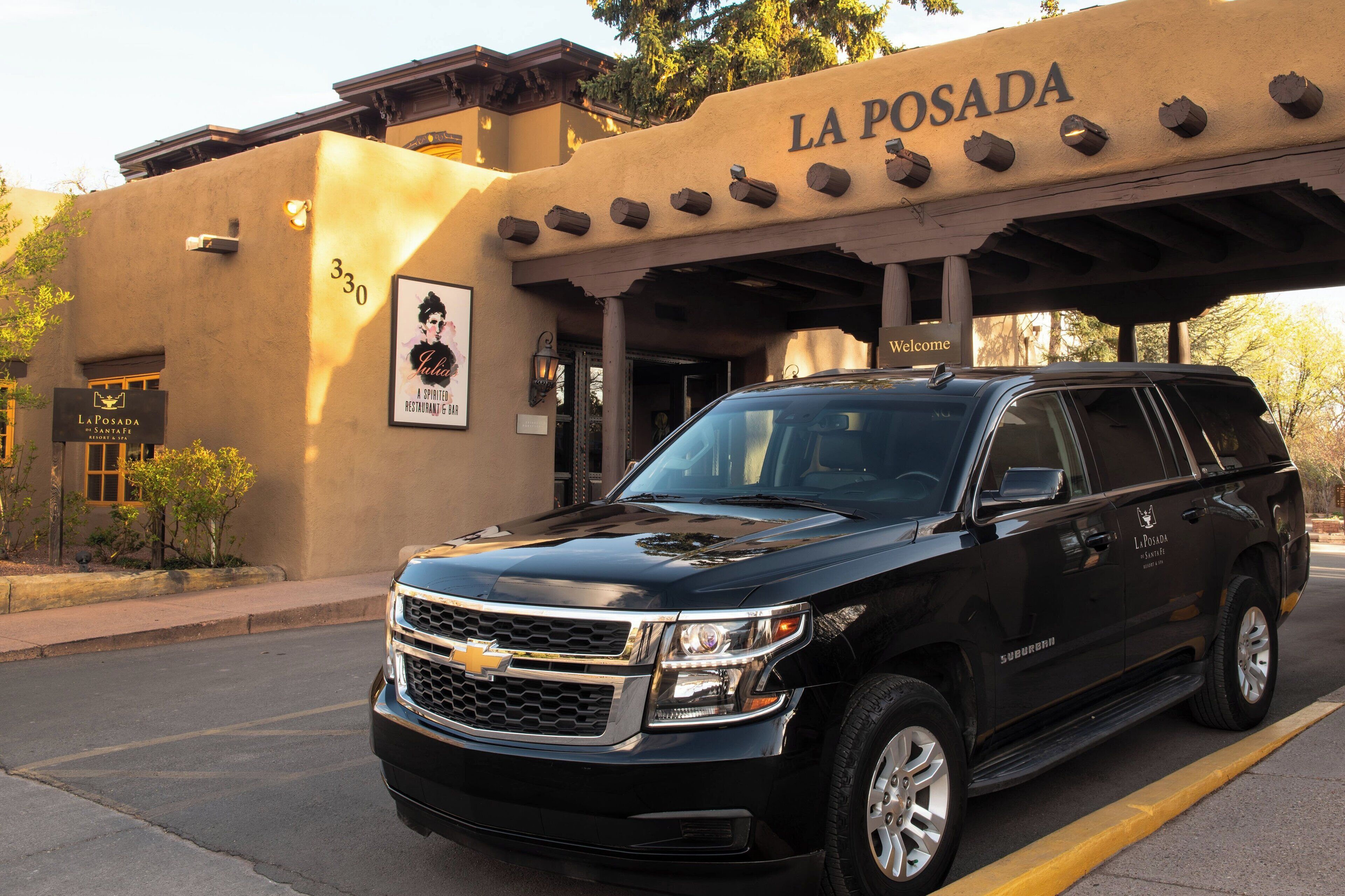 A black Chevrolet Suburban parked in front of La Posada, a building with a beige facade and a sign that reads "Welcome".