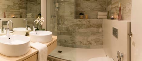 A modern bathroom with two sinks, a glass-enclosed shower, and a toilet.