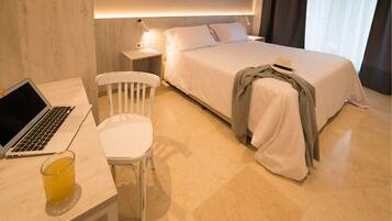 Quarto de hotel com cama, escrivaninha com laptop, cadeira e mesa de cabeceira com abajur.