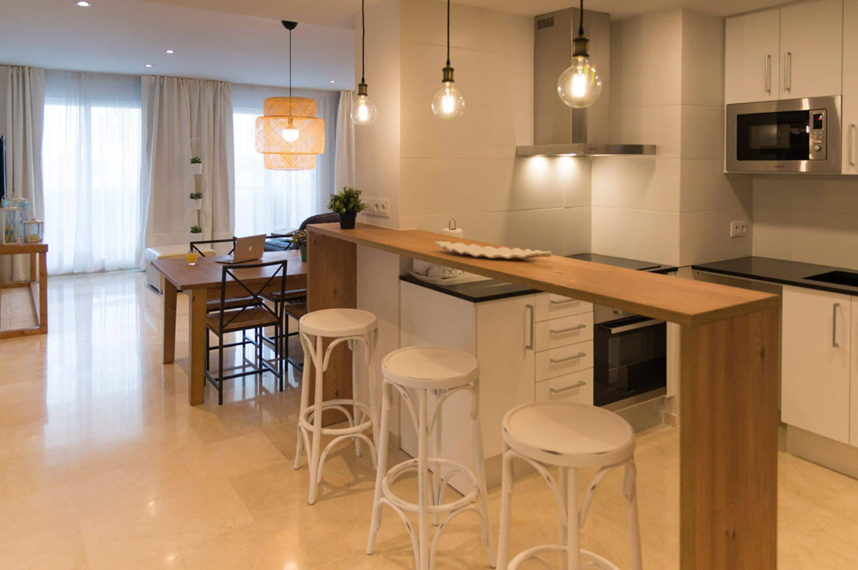 A modern kitchen with a wooden island, bar stools, a built-in oven, and pendant lighting.