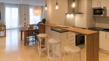 A modern kitchen with a wooden island, bar stools, a built-in oven, and pendant lighting.