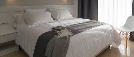 A neatly made bed with a grey throw blanket and a small item on it. There are two wall-mounted lights on either side of the bed.