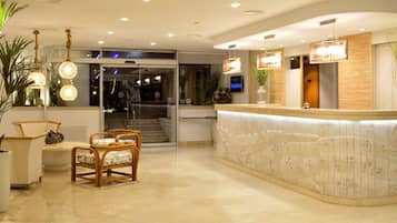 Un'area reception di un hotel con una scrivania a forma di arco, una zona con sedute e piante in vaso.