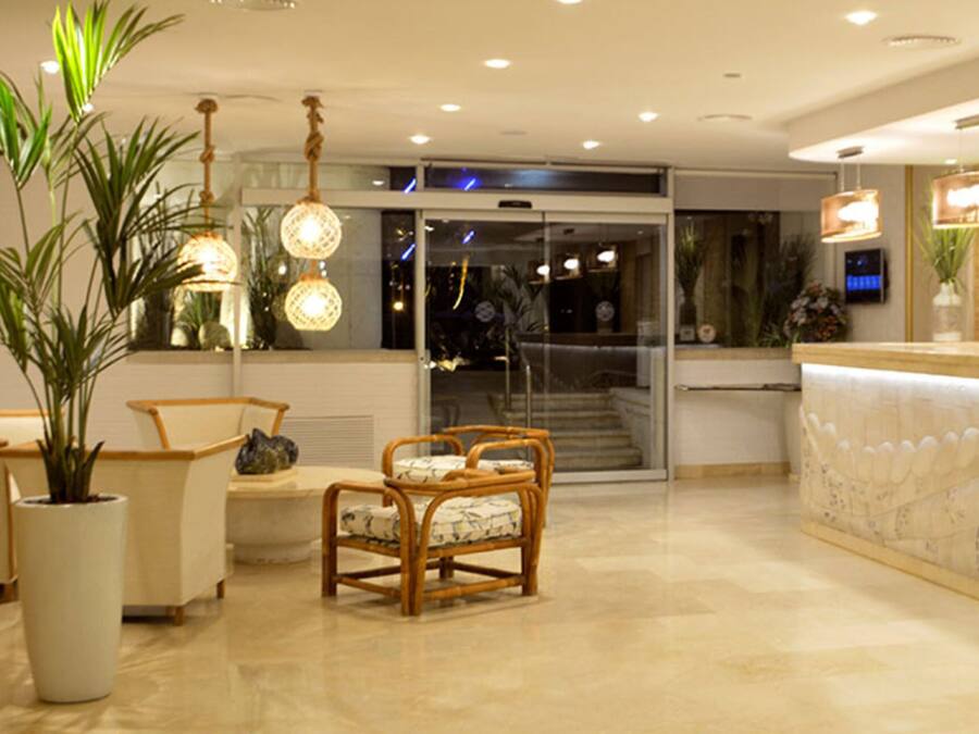 A hotel reception area with a curved reception desk, seating area with chairs, and potted plants.
