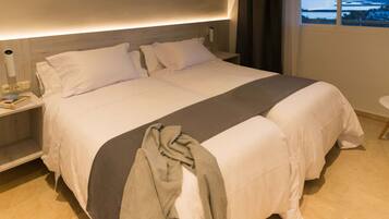 A large bed with white linens, a grey throw blanket, and a bedside table with a lamp.
