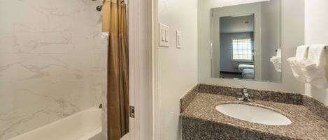 A bathroom with a marble shower wall, a bathtub, a toilet, and a granite sink with a mirror above it.